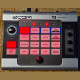 Stříbrný vokálový procesor značky ZOOM, model V3 Vocal Processor. Zařízení má řadu červeně podsvícených tlačítek s bílými nápisy, jako jsou HARMONY,…