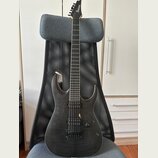 Černá elektrická kytara s tmavým dřevěným povrchem a dvěma humbuckery. Na hlavě hрифu je bílý nápis Ibanez. Nástroj je vybaven pákou tremola a jedním…