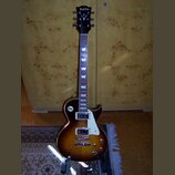 Elektrická kytara s tónem sunburst, bílým pickguardem a dvěma humbuckery. Na hlavě je nápis BaCha a pod ním logo ve tvaru stylizovaného písmena V. Hр…