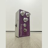 Kytarový efekt pedál s fialovým povrchem a stříbrným kovovým šasi. Na přední straně jsou tři ovládací knoflíky s nápisy LEVEL, GAIN a TONE, jeden sti…