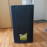 Černý reproduktor s kovovou mřížkou v六úhlíkovém vzoru. V dolní části je nalepená žlutozelená nálepka s nápisy „db technologies“, „BOOST IT LOUDER!“,…