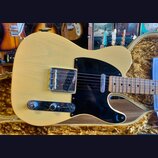 Kytara typu Telecaster v krémové barvě s černým pickguardem a hnědým javorovým hmatníkem. Na kovovém krytu snímače je nečitelný nápis. Nástroj leží v…