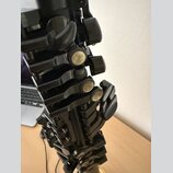 Detailní záběr na mechanismus černého dechového nástroje, pravděpodobně klarnetu. Jsou vidět kovové klapy s perleťovými vložkami a černé plastové neb…