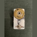 Kytarový efekt pedál s kovovým stříbrným šasi. Na horní části je umístěno velké žluté kolečko s nápisem TONE WHEEL GUITAR PEDAL SERIES BY SALVATION A…