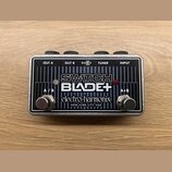 Kytarový pedál v kovovém stříbrném šasi s černým čelem. Na povrchu jsou nápisy SWITCH BLADE+, electro-harmonix a NEW YORK CITY, USA. Jsou zde dva kov…