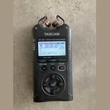 Černý digitální nahrávač s nápisy TASCAM a DR-40X Linear PCM RECORDER. Zařízení má LCD displej s zobrazením času a vlnové formy, horní mikrofony a ov…