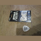 Sada kytarových trzelíků v originálním balení a jeden samostatný trzelík. Na černém obalu je bílý nápis METALLICA WHITE FANG CUSTOM FLIGHT PICK. Samo…