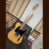Elektrická kytara s přírodním dřevěným povrchem těla a černým pickguardem. Na hlavě hředu je viditelné logo Fender. Kytara má dva snímače, chromovaný…