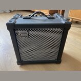 Černý kombo zesilovač s kovovou mřížkou reproduktoru. Na přední straně je umístěno logo a nápis Roland. Horní strana obsahuje ovládací prvky a přenos…