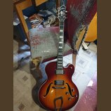 Polodublová elektrická kytara s červeně-žlutým sunburst povrchem a f-otvory. Na hlavě je bílý nápis „Kay Raven“. Kytara má dva snímače, tři ovládací…