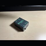 Černý kovový efekt pedál s nápisy v zelené barvě. Na horní straně je logo a název Bespeco a model DBX-10. Na boku jsou viditelné popisky vstupů a výs…