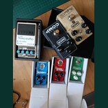 Fotografie zobrazuje šest kytarových efektů. V horní části jsou MXR Super COMP v černé barvě, MXR Custom Badass Modified OD v zlatovém provedení a BO…