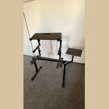 Černý kovový stojan s dvěma plochými deskami, pravděpodobně pro klavír nebo synthesizer. V horní desce je vyfrézovaný obdélníkový otvor. Konstrukce o…