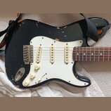 Černá elektrická kytara typu Stratocaster s bílým pickguardem a hnědým hmatníkem. Na každém ze tří snímačů je nápis "Made in USA". Lak na těle kytary…