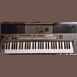 Šedý elektronický klavír s bílými a černými klávesami. Na horní části je uprostřed logo YAMAHA, displej a po obou stranách mřížkovité reproduktory. V…