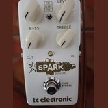 Bílý kytarový efekt s nápisem SPARK BOOSTER a logem tc electronic. Na horní straně jsou čtyři bílé otočné knoflíky s popisky LEVEL, BASS a TREBLE, dá…