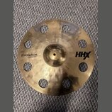 Zlatý kovový činel s otvory v okruhu kolem středu. Na povrchu jsou nápisy Evolution, O-Zone Crash 15" 40 cm a HHX. Povrch vykazuje jemné rýhy a drobn…