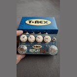 Kytarový efekt s nápisem T-REX REPLAY BOX Delay a doplňkem Made by T-REX Denmark. Zařízení má šedý povrch, čtyři bílé ovládací knoflíky s popisky VOL…