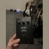Černý kytarový výkonový zesilovač s nápisem Harley Benton GPA-100 Guitar Power Amplifier. Na horní straně jsou tři menší otočné ovladače s popisky BA…