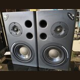 Dva šedé studiové reproduktory značky Alesis. Každý obsahuje jeden výškovej reproduktor, dva bassreflexní otvory a jeden basový reproduktor s nápisem…