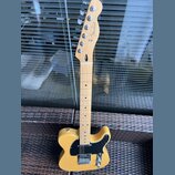 Žlutá elektrická kytara typu Telecaster s černým pickguardem. Na hlavě hředu je viditelné logo Fender a nápis TELECASTER. Nástroj vykazuje známky pou…