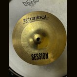 Zlatavý kovový činel s nápisem istanbul® a pod ním menším písmem Mahmet Handmade Cymbals from Turkey. Ve spodní části je uveden model SESSION. Činel…
