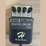 Šedý kytarový efekt s nápisem DIGITAL DELAY DD-2 a logem Harley Benton. Na horní straně jsou čtyři černé otočné ovířky s popisy VEL, K, M a časovým r…