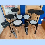 Elektronická bicí souprava s černými pady a činely. Na všech bílých plochách padů je vidět nápis Roland V-Drums. Součástí sestavy je ovládací modul,…