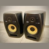 Dva černé studiové monitory s žlutými membránami basových reproduktorů. Na přední straně každého z nich je zlaté logo KRK a bílý nápis VXT8. Povrch j…
