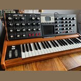 Synthesizér s klaviatura v dřevěném šasi. Na horním ovládacím panelu jsou nápisy LFO, MODULATION BUSSES, OSCILLATORS, MIXER, FILTERS, ENVELOPES a OUT…