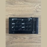 Černý analogový syntetizátor s nápisem WERKSTATT-01 ANALOG SYNTHESIZER a logem moog. Přístroj obsahuje různé ovládací knofíky, přepínače a sekce ozna…