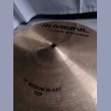 Kruhová mosazná činely s koncentrickým žebrováním. Na povrchu je černý nápis MEINL LIVE SOUND a v dolní části text 14" MEDIUM HI-HAT TOP. Povrch vyka…