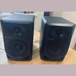 Dva černé studiové reproduktory s hranatým tvarem. Na přední straně každého reproduktoru je bílý nápis Pioneer DJ, nadstavba s výškým reproduktorem a…