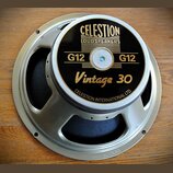 Reproduktor s kovovým rámem stříbrné barvy a černým krytem magnetu. Na krytu je zlatý nápis CELESTION LOUDSPEAKERS, G12 G12 a Vintage 30, v dolní čás…
