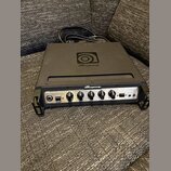 Černý basový zesilovač značky Ampeg s nápisem PortaFlex. Na horní straně je umístěno logo Ampeg. Přední panel obsahuje ovládací knofíky, přepínač -15…
