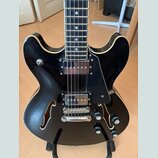 Černá polodublová elektrická kytara s bílým lemováním hran. Nástroj má dva humbuckery, černý plech (pickguard) a čtyři ovládací knoflíky. Na těle jso…