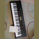 Černý digitální klavír s bílými a černými klávesami. Na ovládacím panelu je nápis CTK-3500 a logo CASIO. K nástroji přikládaný papírový dokument nese…