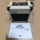 Kremový kytarový kombo zesilovač s černou mřížkou reproduktoru a nápisem VOX na přední straně. Na horním ovládacím panelu jsou různé přepínače a pote…