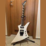 Bílá elektrická kytara s ostře hranatým tvarem těla a špičatou hlavou. Na hlavě je viditelné logo Jackson. Kytara má dva černé humbuckery, dvě ovláda…