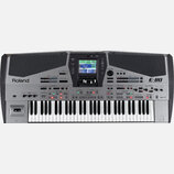 Stříbrný digitální klavír s černými mřížkovými panely v horní části. Na levé straně je nápis Roland a na pravé straně označení E-80 MUSIC WORKSTATION…