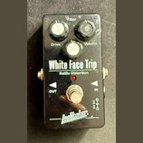 Černý kytarový efekt s nápisy White Face Trip a Rattle Distortion. Na horní straně jsou tři černé otočné ovladače s popisky Filter, Drive a Volume. V…