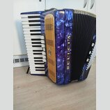 Modrá akordeon s mramorovaným povrchem a zlatou mřížkou. Na boku je svisle napsaný nápis DELICIA a na mřížce se nachází malý oválný štítek s nápisem…