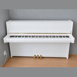 Bílé digitální piano s klaviatura a uzavíracím víkem. Na levé straně nad klávesami je viditelné kulaté logo, které je však nečitelné. Nástroj má zlat…