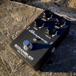 Černý kytarový pedál s nápisem SCRAMBLER Bass Overdrive a logem Ampeg. Na horní straně jsou čtyři černé otočné knoflíky s popisky Drive, Blend, Trebl…