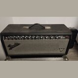 Kytarový zesilovač v černém krytu s kovovou rukojetí. Na ovládacím panelu jsou nápisy INPUT, VOLUME, TREBLE, BASS, GAIN, VOLUME, TREBLE, MID, BASS, R…