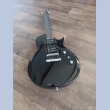 Černá elektrická kytara s tvarem připomínajícím model Les Paul. Nástroj má dva humbuckery, Tune-o-matic můstek a dvě ovládací knoflíky. Povrch je les…