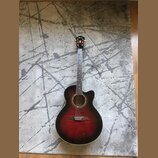 Akustická kytara s vyřezem (cutaway) v červenohnutém sunburst provedení. Na hlavě je viditelné logo Ibanez. Hриф má bílé polohovací značky a kytara j…