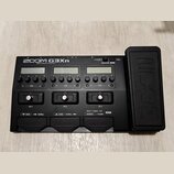 Černý kytarový efektový procesor s nápisem ZOOM G3Xn Multi-Effects Processor. Zařízení má tři LCD displeje, několik ovládacích knoflíků a tři spodní…