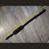 Černý popruh na hudební nástroj z textilního materiálu s širší středovou částí. Popruh je položen vedle žlutého skladovacího metru na šedé podlaze. N…