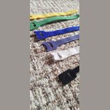 Šest kusů textilních pásků s otvorem na jednom konci, položených vedle sebe na koberci. Pásky jsou v barvách žluté, zelené, modré, fialové, bílé a če…